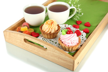 Cups of tea with cakes on wooden tray isolated on white
