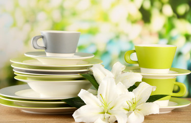 Empty plates and cups on wooden table on green background