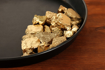 Gold pan with golden nuggets inside on wooden background