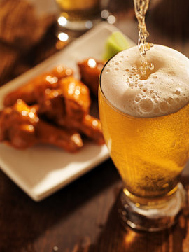 pouring beer with chicken wings in background.