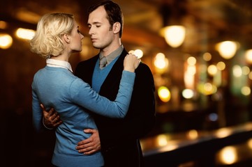 Man in jacket embracing woman in blue cardigan outdoors at night