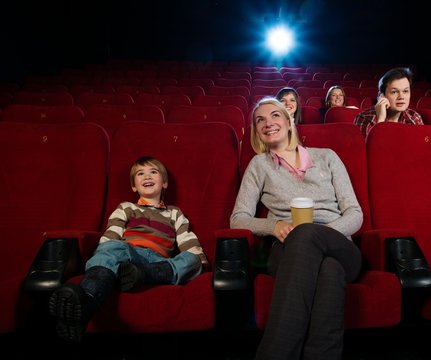 Smiling mother and her son in cinema with other people behind th