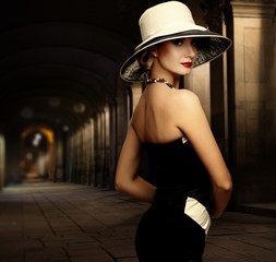 Woman in black dress and big white hat alone outdoors at night