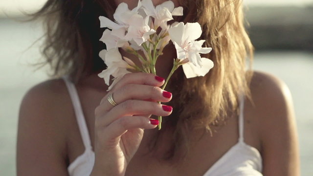 Young woman standing on seashore and smelling flower, slow motio