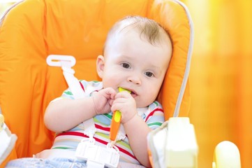 The baby sits on chair and holds spoon