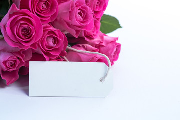 Bouquet of beautiful pink roses with an empty card on a table