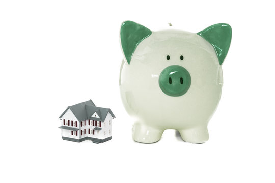 Green piggy bank standing beside miniature home