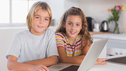Two children looking at the camera together with laptop in front