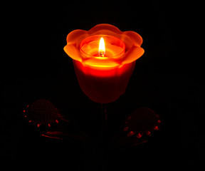 a burning candle in a candlestick in the form of a rose on a bla