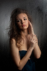 Portrait of a girl behind wet glass on a gray background.