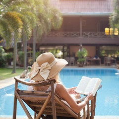 woman reading book in deck chair near swimming pool