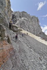 People are climbing toward a mountain pass in the Dolomites