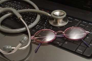  stethoscope and glasses rest on keyboard notebooks