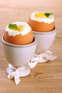 Boiled eggs in egg cups, on wooden table