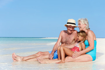 Grandparents With Granddaughter Enjoying Beach Holiday