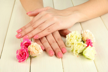 Obraz na płótnie Canvas Kobieta ręce z różowym manicure i kwiatów, na drewnianych