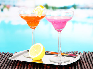 Glasses of cocktails on table near pool