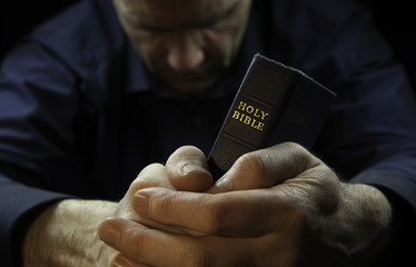 A Man praying holding a Holy Bible. - obrazy, fototapety, plakaty