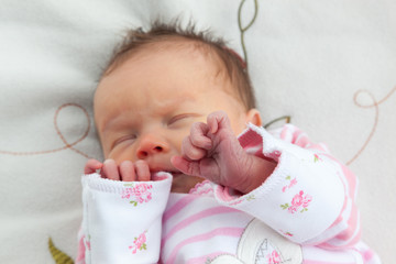Newborn baby girl clutching her hands to her face