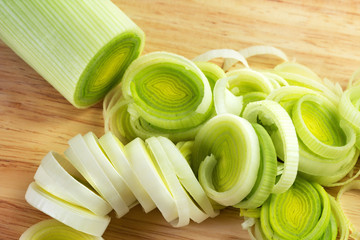 Fresh leeks whole and sliced on a wooden bread board