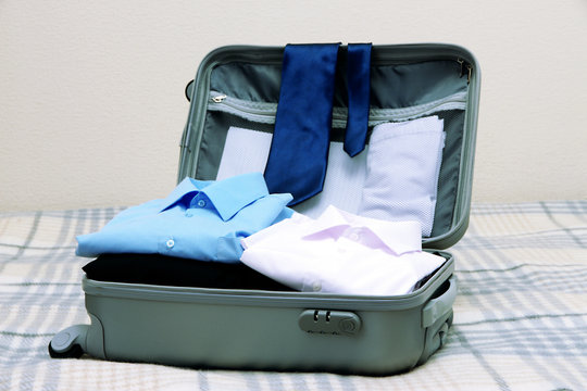 Open grey suitcase with clothing on bed