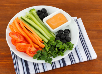 Assorted raw vegetables sticks in plate on wooden table close