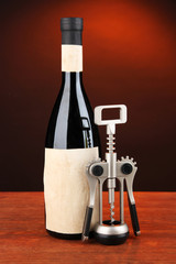 Corkscrew and bottle of wine on wooden table, on dark