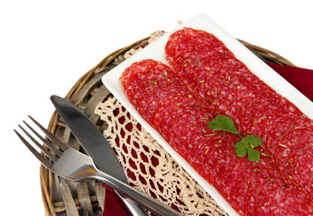 Tasty salami on plate on  wicker cradle isolated on white