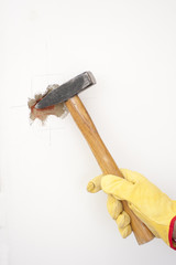 Hammer smashing hole in white home wall