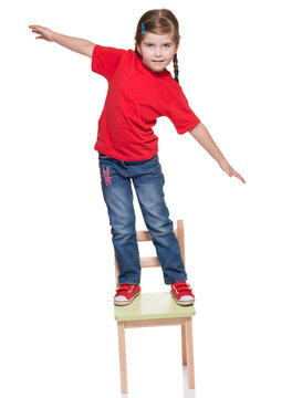 littlr gitl standing on a chair and balancing