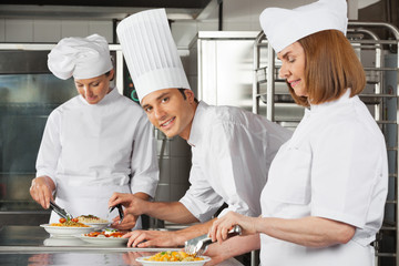 Male Chef With Colleagues Working In Kitchen