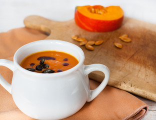 Pumpkin vegetable cream soup in white bowl with piece pumpkin