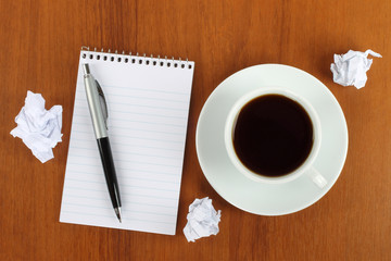Cup of coffee with notepad, pen and crumpled paper