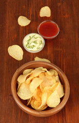 Potato chips  in wooden bowl and sauces, on wooden background
