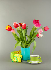 Beautiful tulips in bucket with gifts and cup of tea