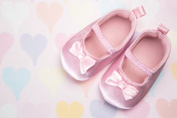 Fototapeta na wymiar Baby pink booties on heart pattern background