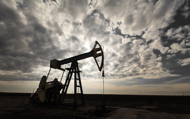 Operating oil well profiled on dramatic cloudy sky