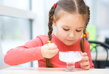 Fototapeta premium Little girl is eating ice-cream in parlor
