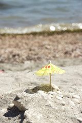 Fototapeta na wymiar Small paper umbrella on beach near sea shells