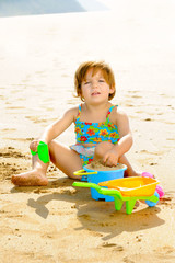 Happy toddler girl playing with her toys on the beach