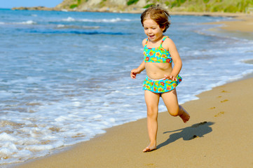 Happy toddler girl running on the beach
