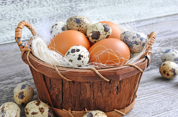 Different types of eggs in a basket on a old wooden background
