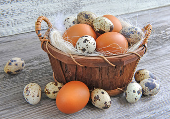 Different types of eggs in a basket on a old wooden background