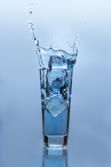 Fototapeta na wymiar Kostka lodu spada w szklance wody