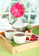 Obraz na płótnie Canvas Filiżanki herbaty z kwiatem i ciasto na drewnianej tacy na stole w