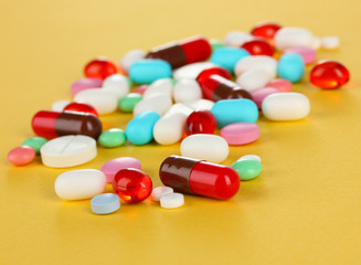 Assortment of pills, tablets and capsules on yellow background