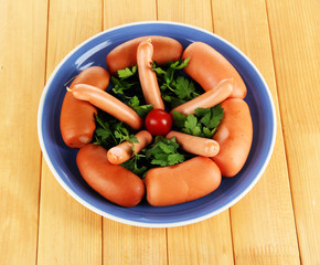 Sausage, greens, tomato on plate on wooden table