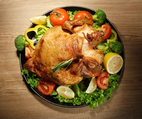 Whole roasted chicken with vegetables on plate, on wooden table