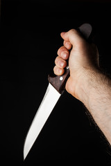 Hairy male hand  holding a knife over a black background
