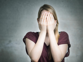 Junge Blondine hält sich die Hände vors Gesicht